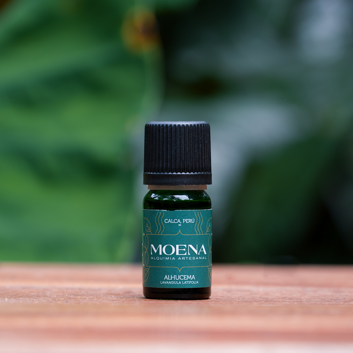 Small bottle of Andean Lavender Essential Oil - Alhucema on a wooden surface against a blurred green plant background
