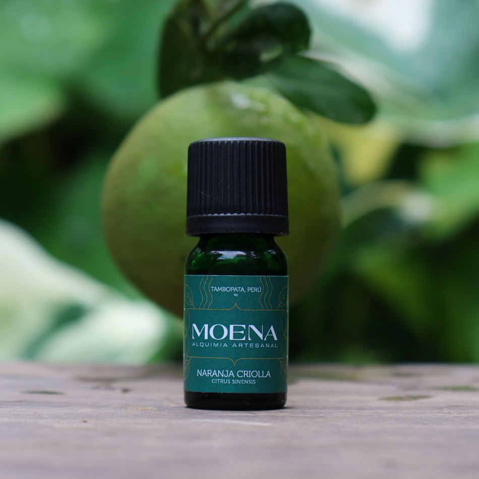 Small green bottle labeled 'Moena'Naranja Creiolla on a wooden surface with a blurred creole orange in background