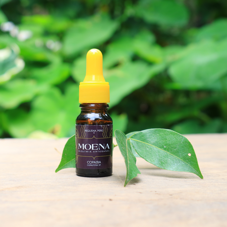 Bottle of Moena Copaiba oil resin with a yellow cap on a wooden surface with green leaves in the background