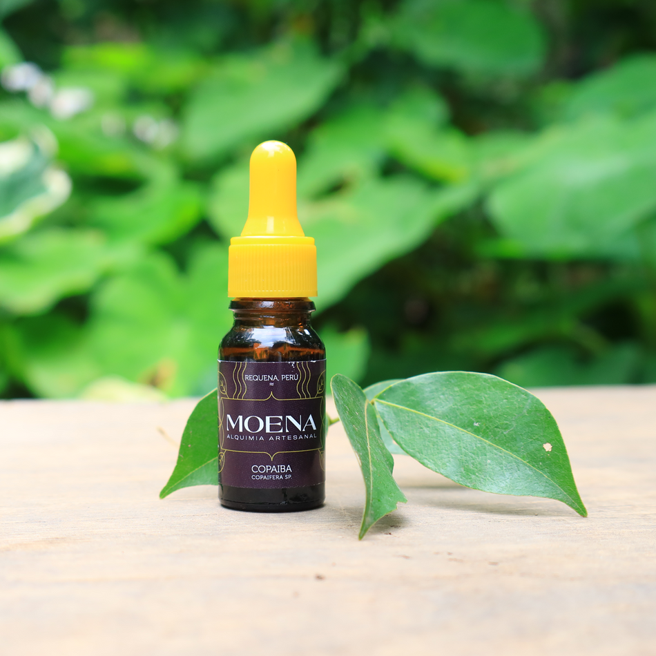 Bottle of Moena Copaiba oil resin with a yellow cap on a wooden surface with green leaves in the background