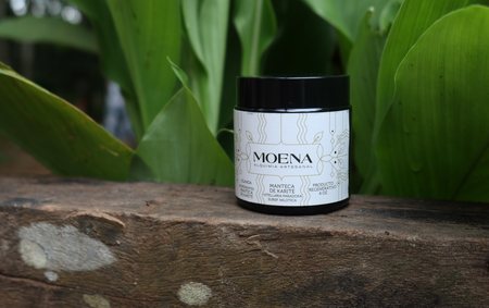 Moena Shea Butter product on a wooden surface with green leaves in the background